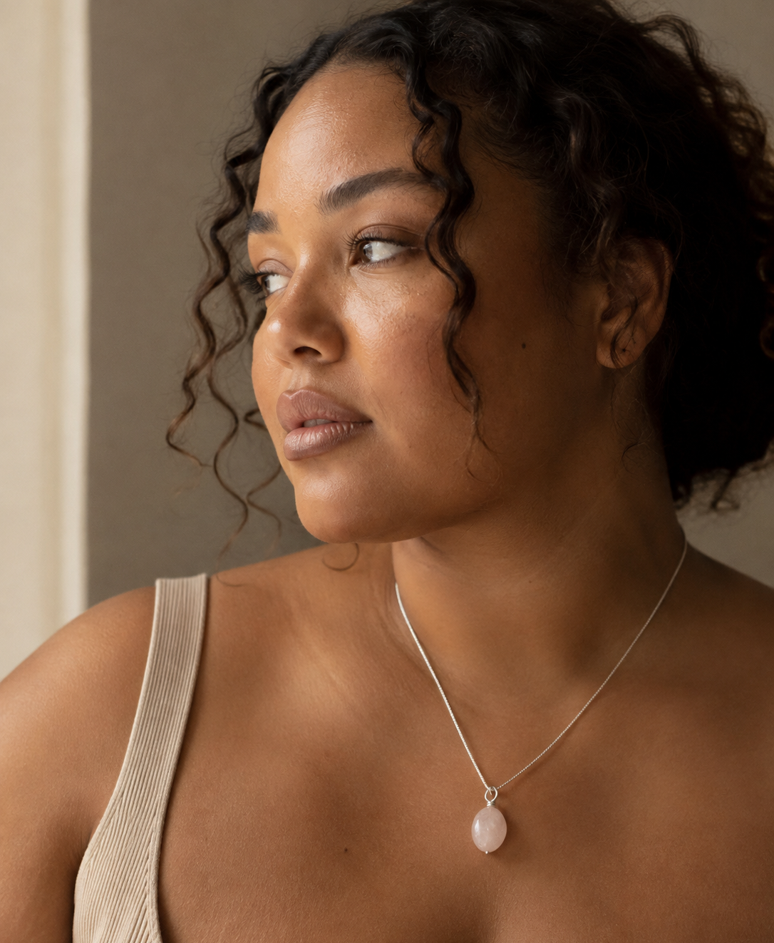 Plus-size mixed-race woman wearing the Rosa Rose Quartz Pendant from Rya Atelier on a fine sterling silver chain in soft natural light. 