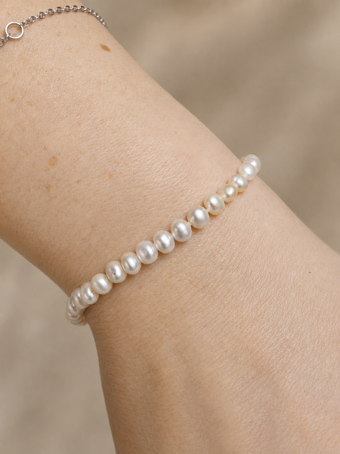 A close-up of a person's wrist wearing a Lulu Bracelet by Ryã Atelier featuring petite 4mm freshwater pearls with sterling silver clasp. 