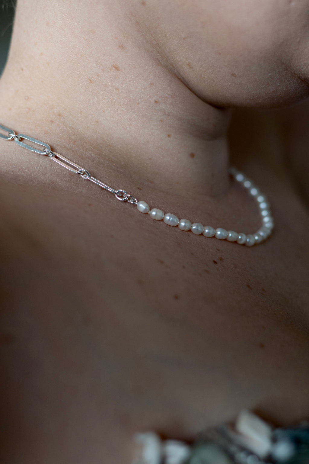 A close up of a model wearing The Ayanda Necklace by Ryā Atelier features a solid sterling silver handmade paperclip chain and a string of delicate freshwater pearls. 