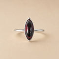 Amanda Ring handcrafted in solid 925 sterling silver featuring a natural marquise cabochon garnet in a bezel setting by Ryã Atelier on a beige background. 
