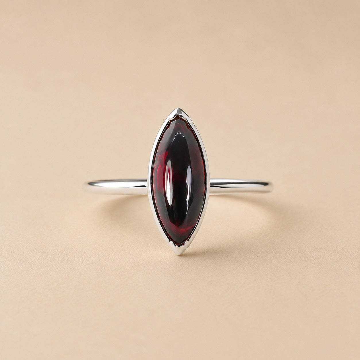 Amanda Ring handcrafted in solid 925 sterling silver featuring a natural marquise cabochon garnet in a bezel setting by Ryã Atelier on a beige background. 