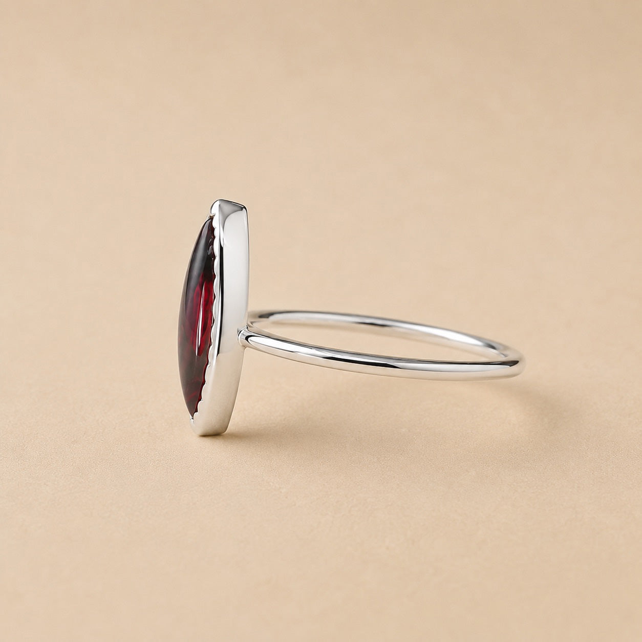 Amanda Ring handcrafted in solid 925 sterling silver featuring a natural marquise cabochon garnet in a bezel setting by Ryã Atelier, on a beige background
