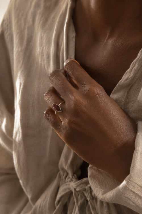 Model wearing the Amanda Ring handcrafted in solid 925 sterling silver with a natural marquise cabochon garnet set in a bezel setting by Ryã Atelier with a beige linen shirt and a blurred background.