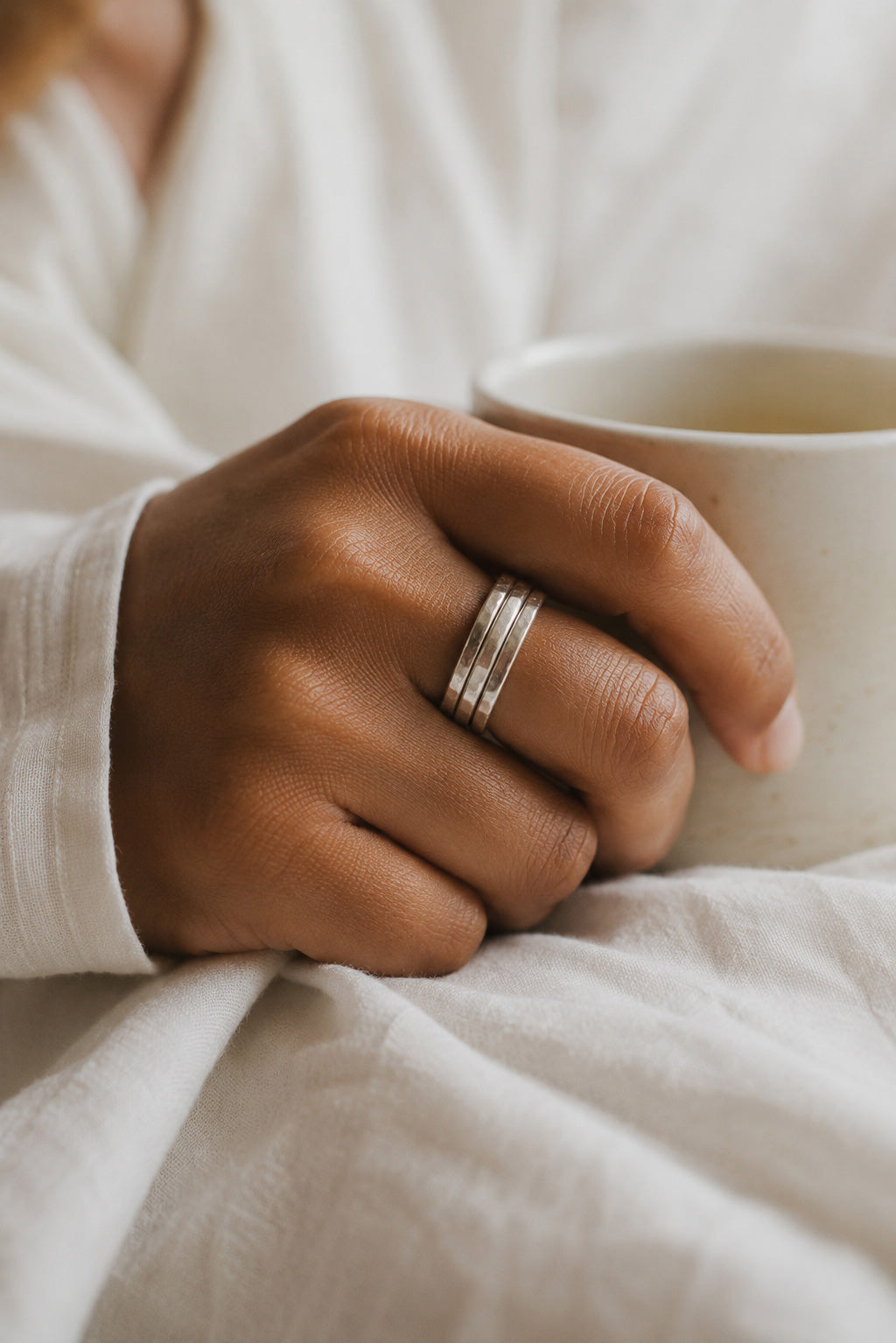 Close up of models hands wearing three Asanda Thick Rings handcrafted in solid 925 sterling silver with hand-hammered faceted bands by Ryã Atelier.