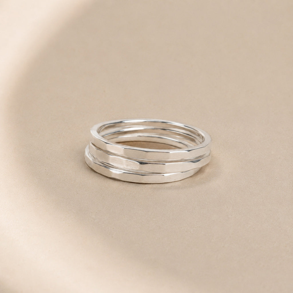 Three Asanda Thick Rings handcrafted in solid 925 sterling silver with hand-hammered faceted bands by Ryã Atelier, on a beige background.
