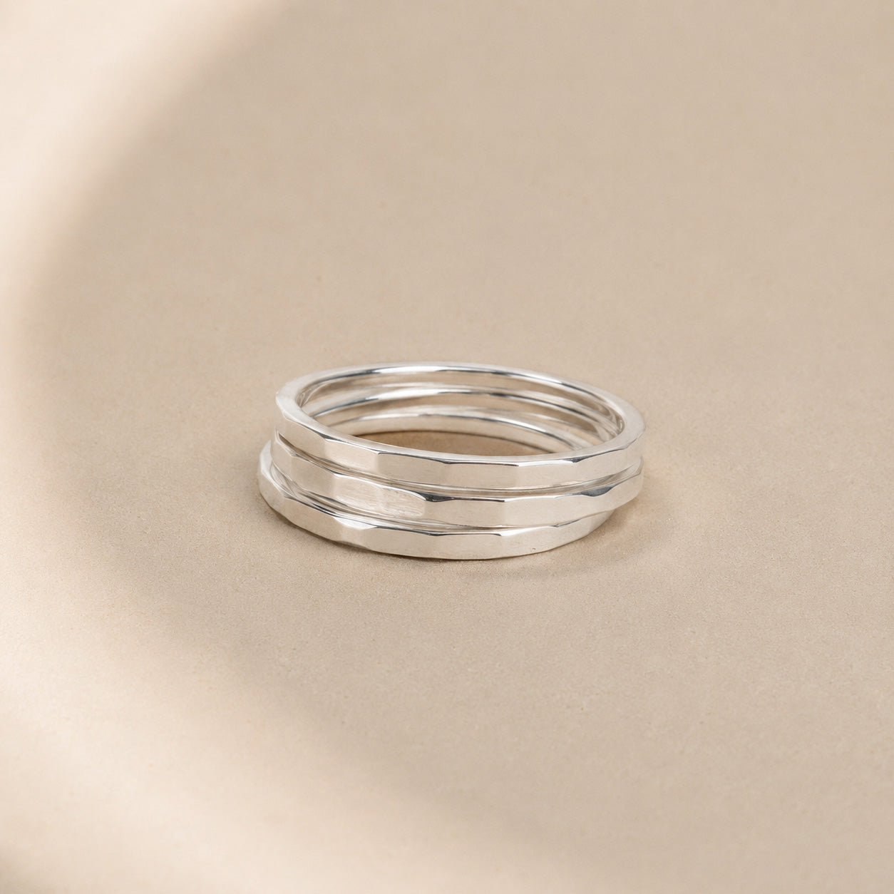 Three Asanda Thick Rings handcrafted in solid 925 sterling silver with hand-hammered faceted bands by Ryã Atelier, on a beige background.