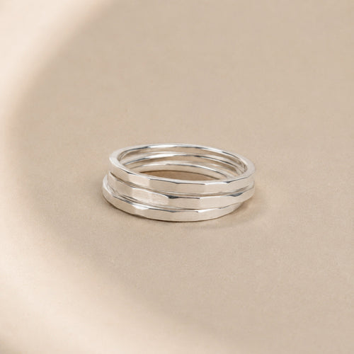 Three Asanda Thick Rings handcrafted in solid 925 sterling silver with hand-hammered faceted bands by Ryã Atelier, on a beige background.