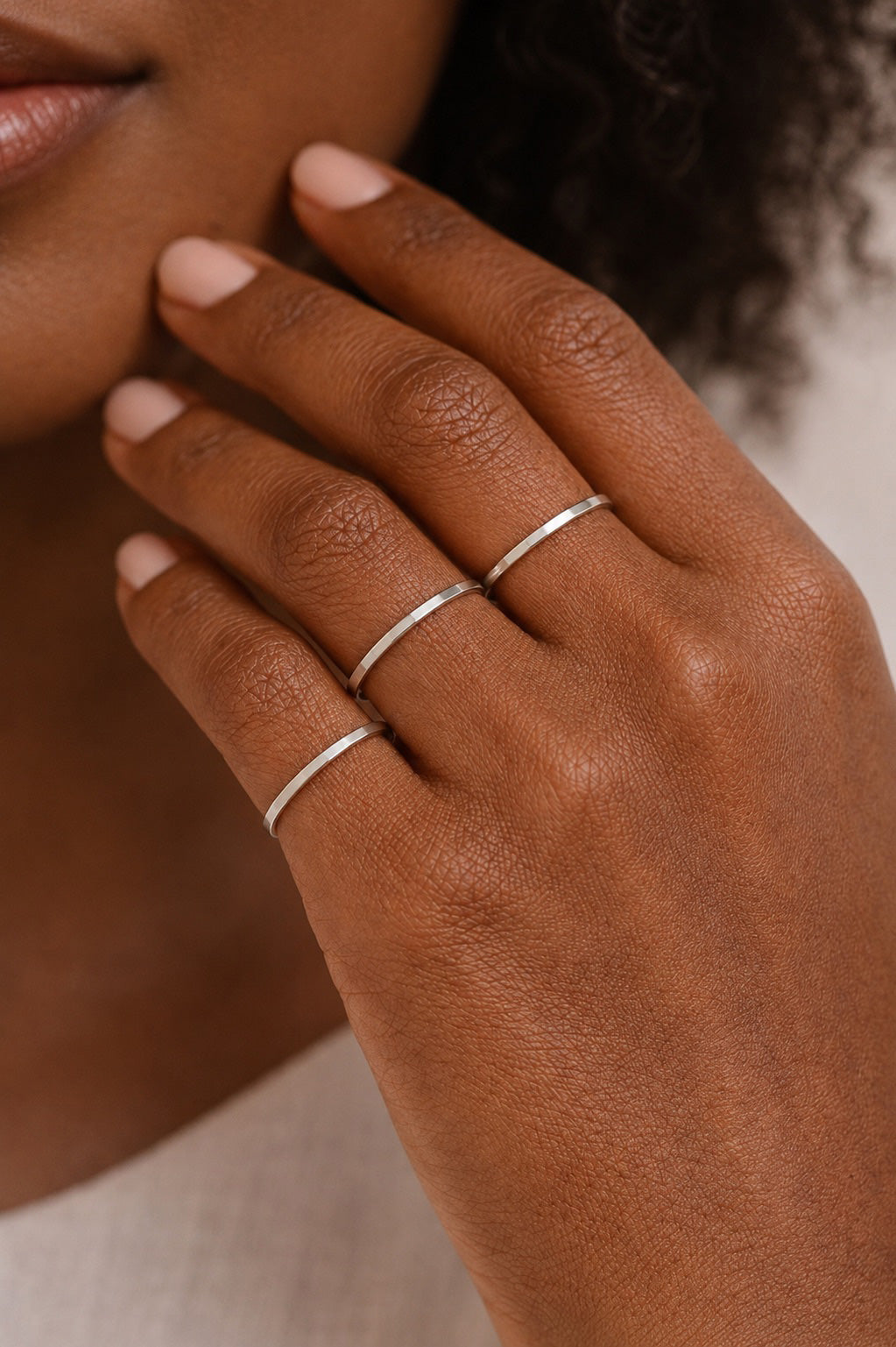 Hand model wearing Three Asanda Thin Rings handcrafted in solid 925 sterling silver with hand-hammered faceted bands by Ryã Atelier, one on each finger.