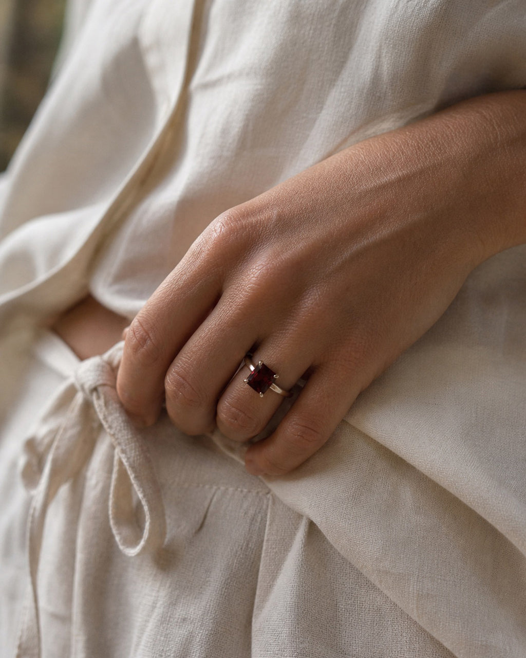 Close up of a hand wearing the Holly Ring handcrafted in solid 925 sterling silver featuring a natural emerald cut garnet in a contemporary four-claw setting by Ryã Atelier.