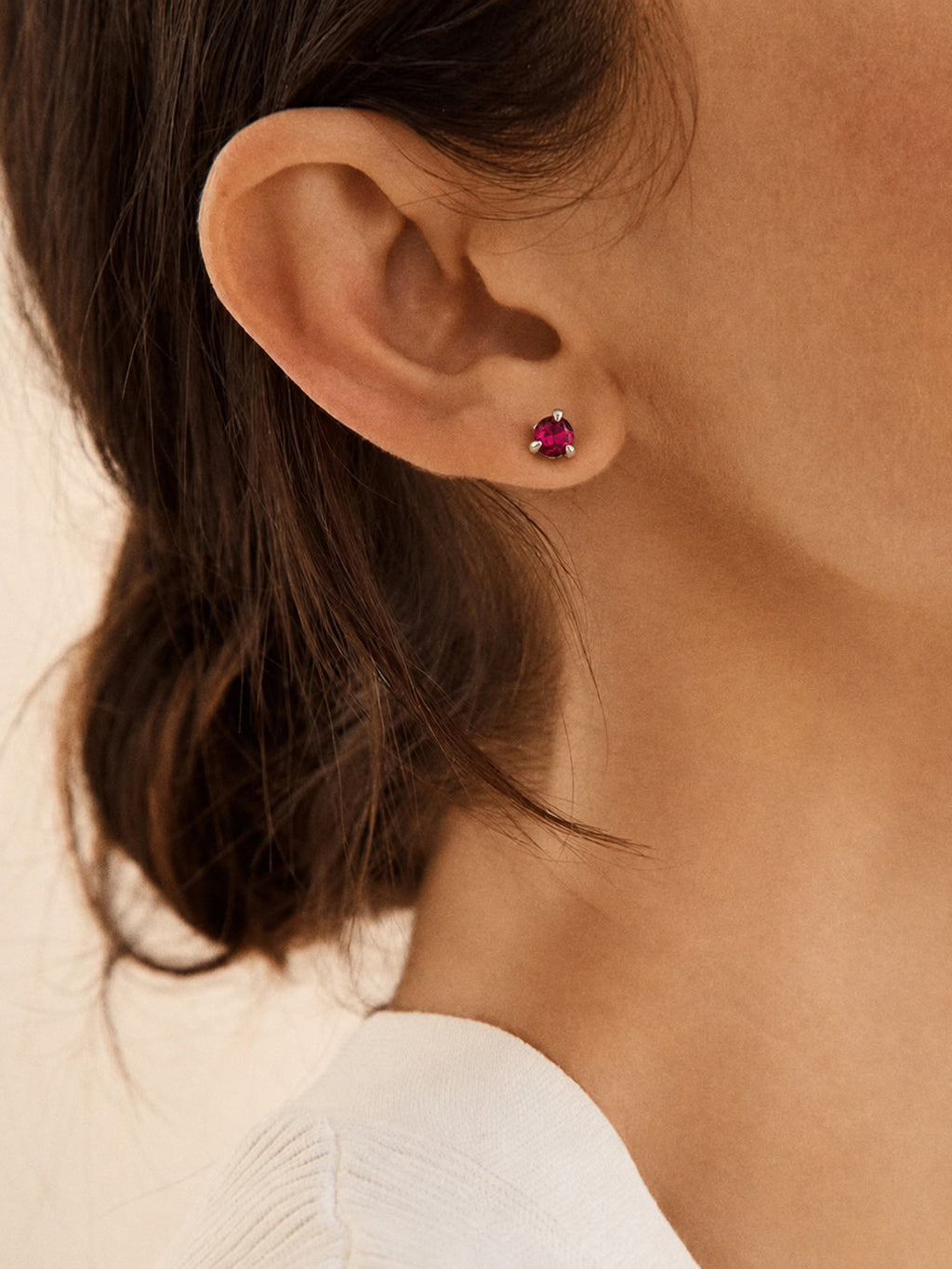 Close-up of an ear wearing a natural garnet earring set in sterling silver with a neutral background