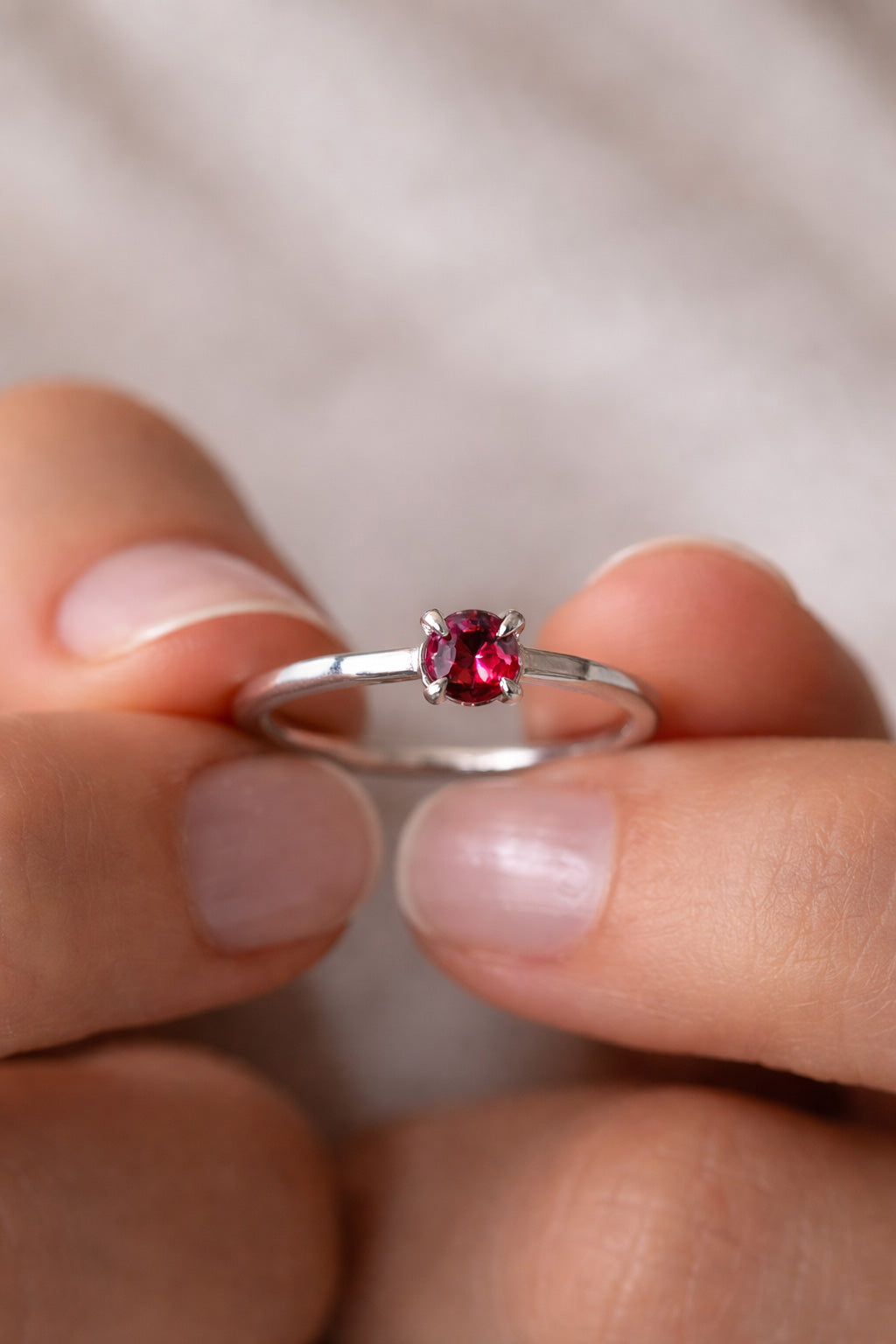 Sterling Silver ring with a natural red garnet held between fingers against a neutral background