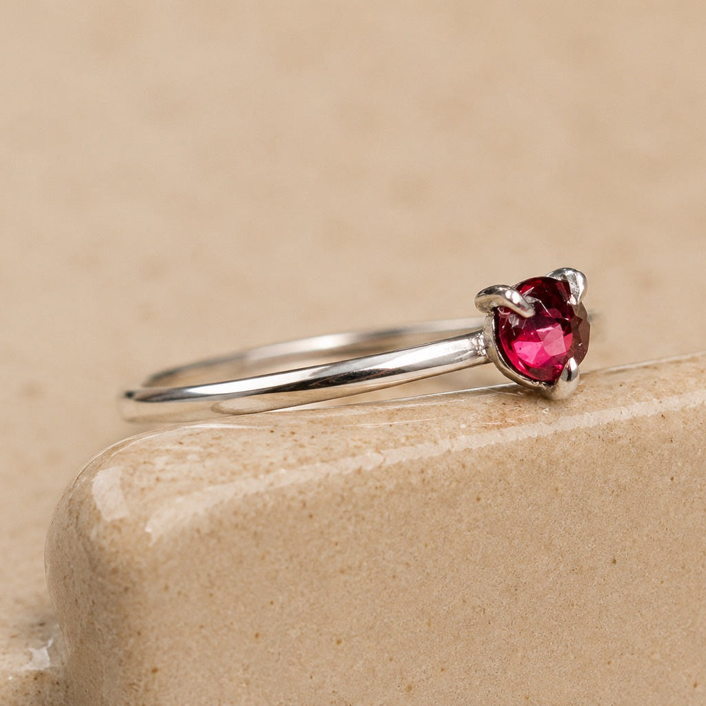 Sterling Silver ring with a red garnet on a beige stone surface