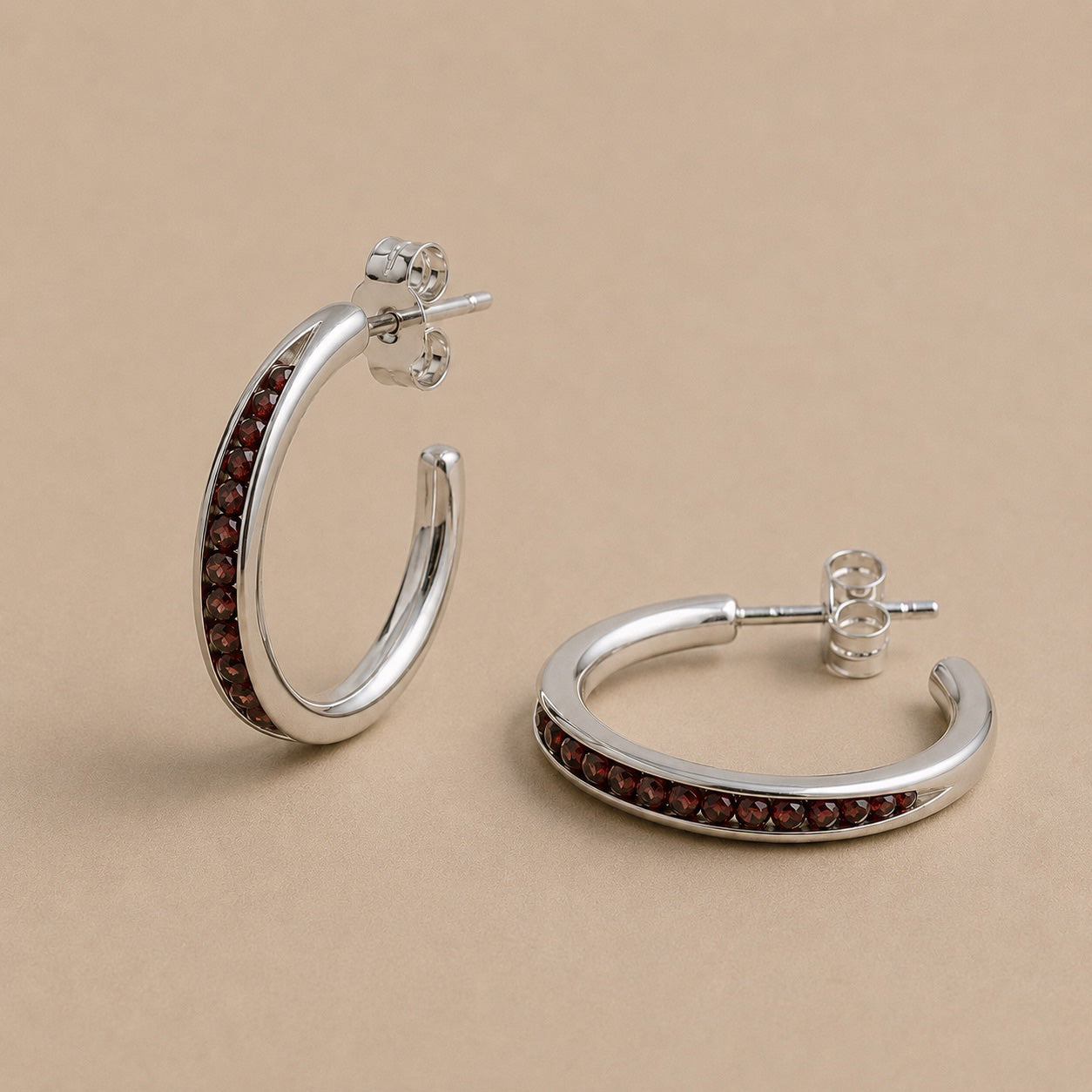 Sterling Silver hoop earrings with garnet beads on a beige background