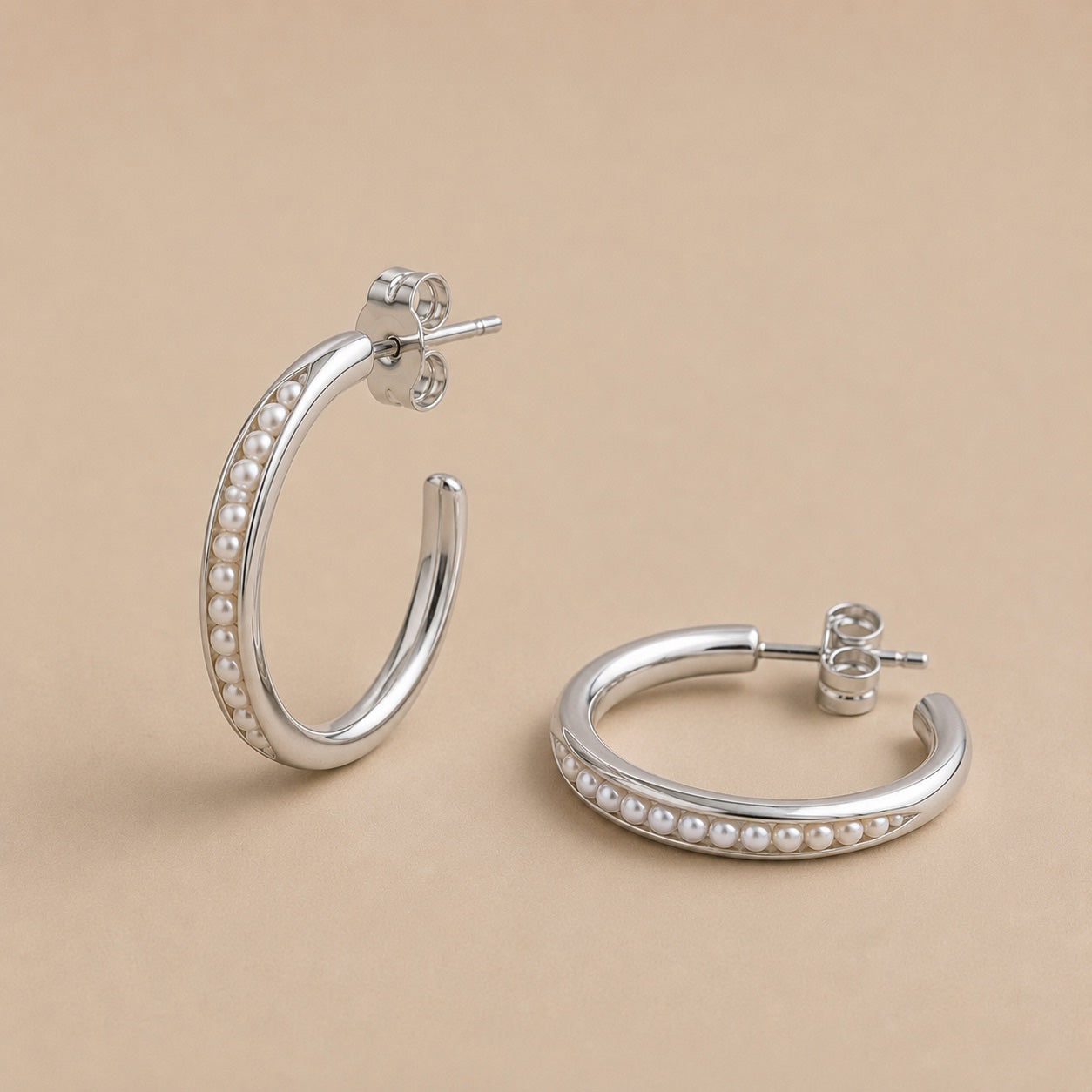 Sterling Silver hoop earrings with freshwater pearl beads on a beige background