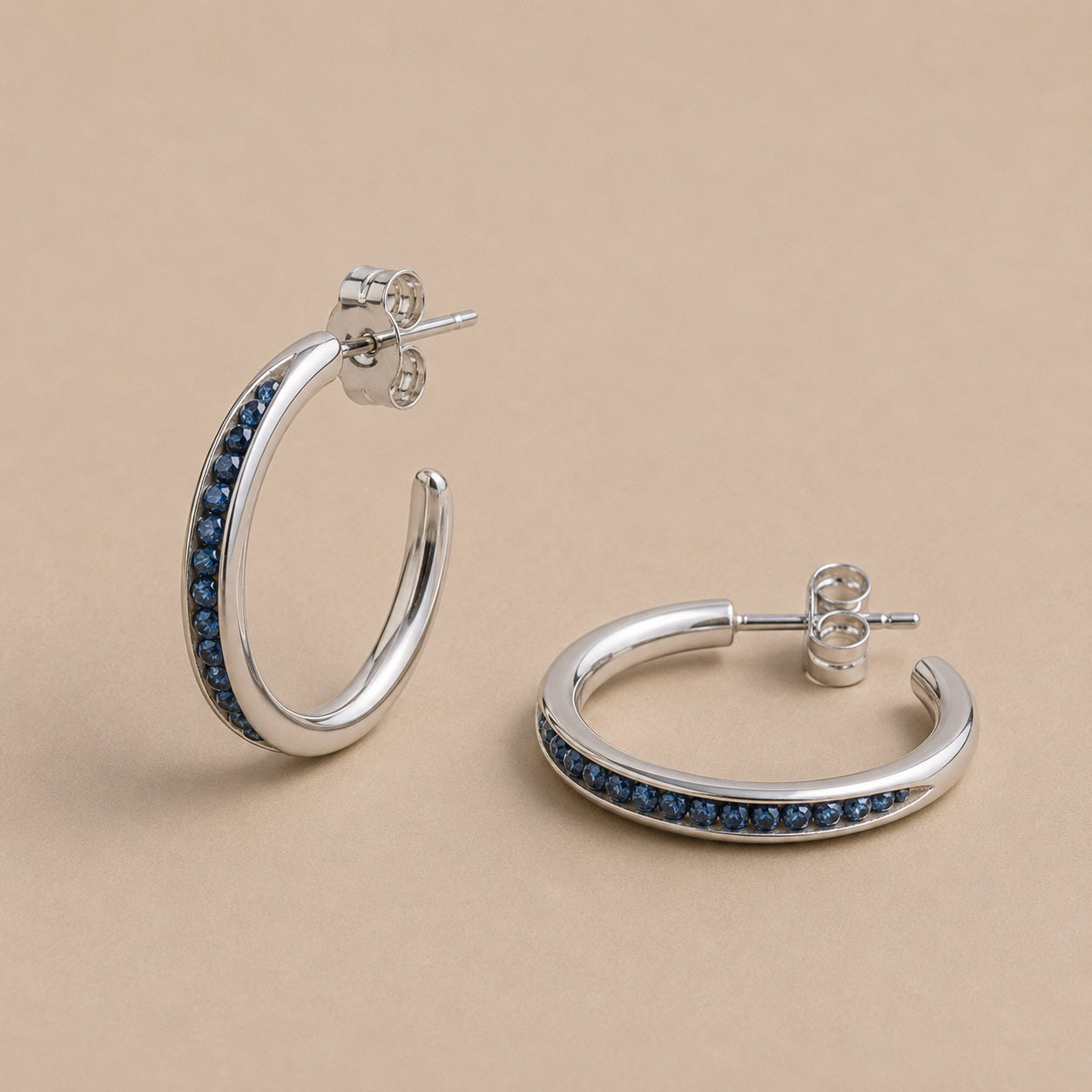Sterling Silver hoop earrings with sapphire beads on a beige background