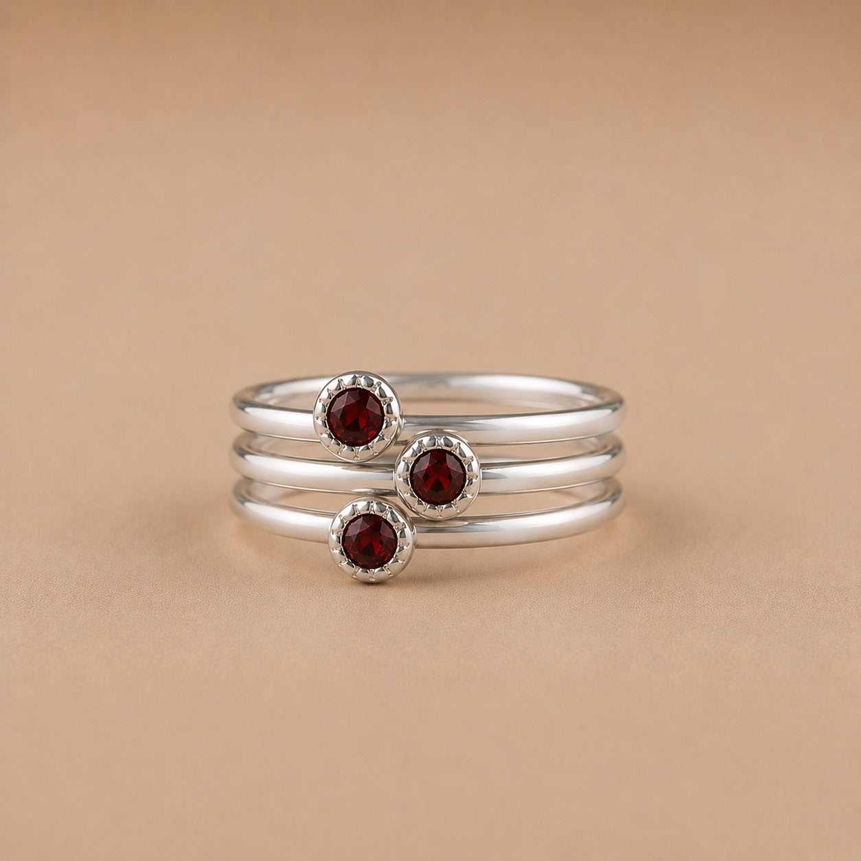 Three sterling silver rings with garnet stones on a beige background