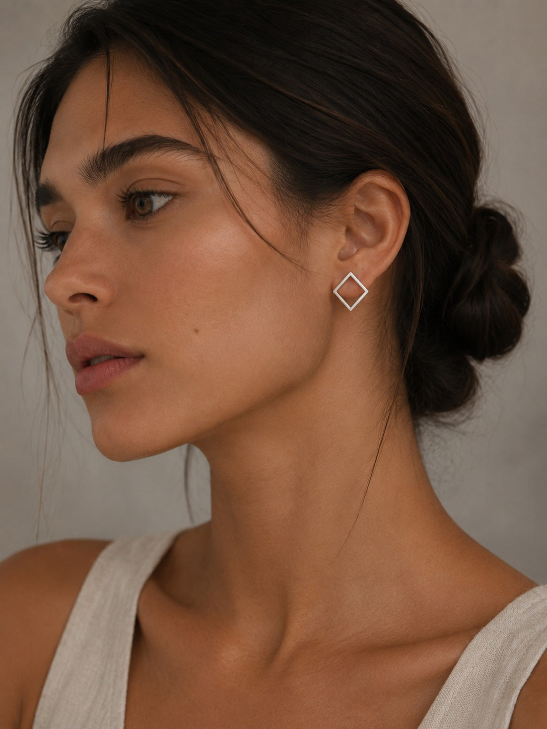 Woman wearing a sterling silver diamond-shaped earring against a neutral background