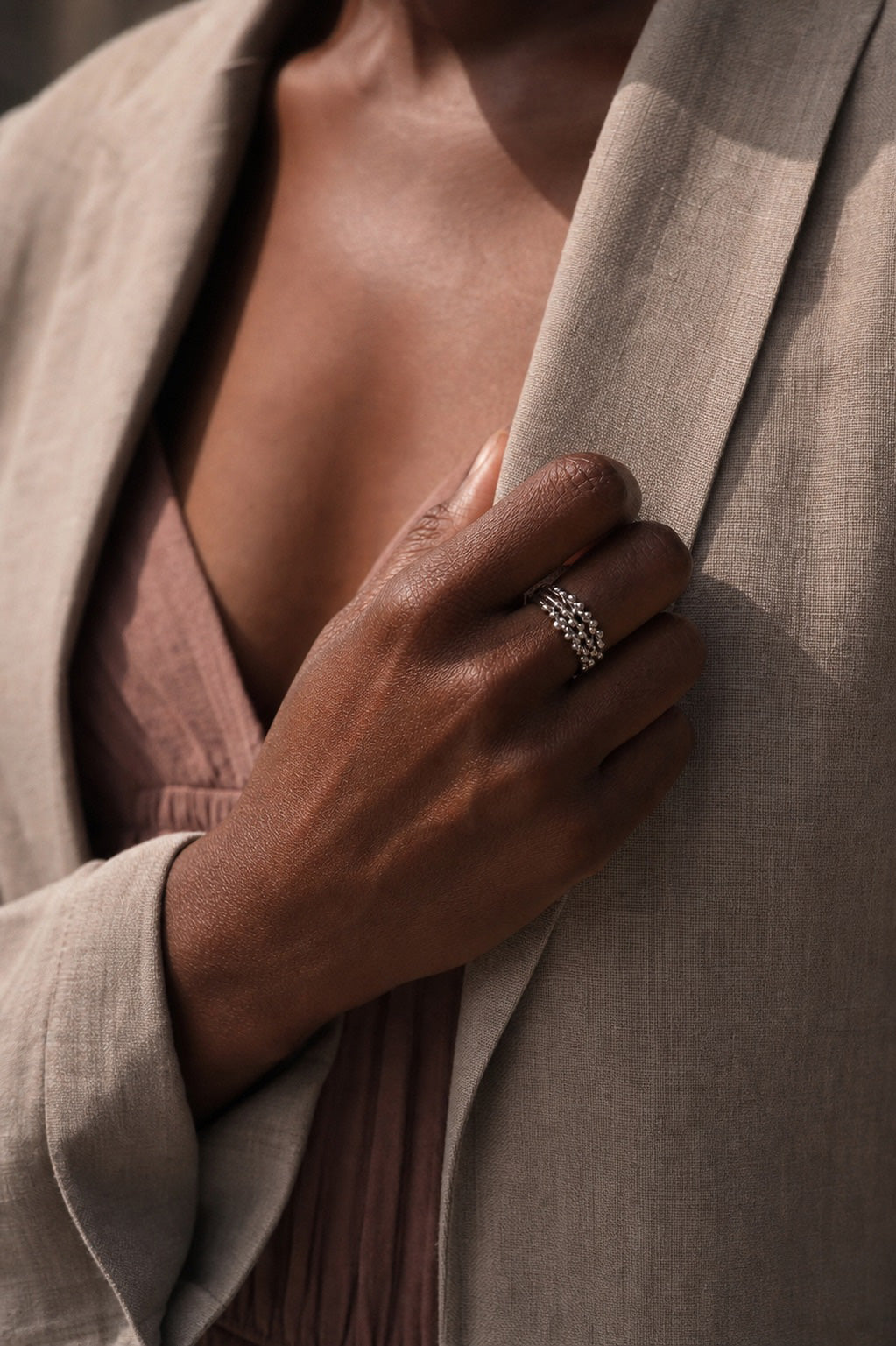 Close-up of a hand wearing 3 stack sterling silver rings with a detailed beaded design, holding a garment.