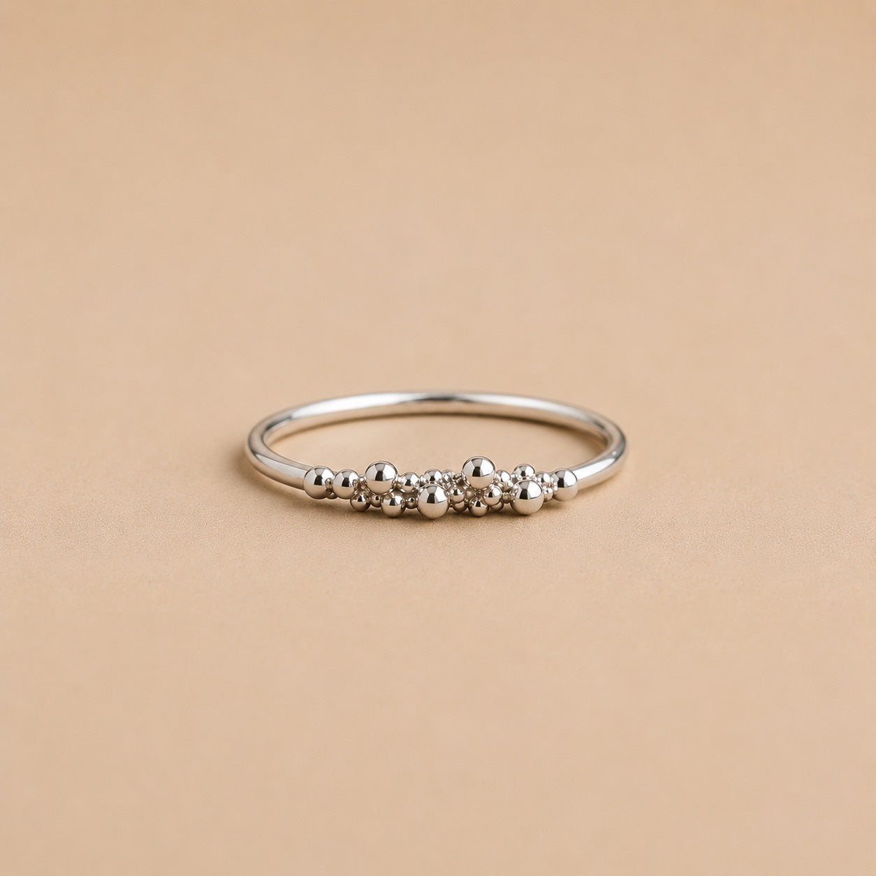 Sterling Silver ring with organic raindrop bead detailing on a beige background