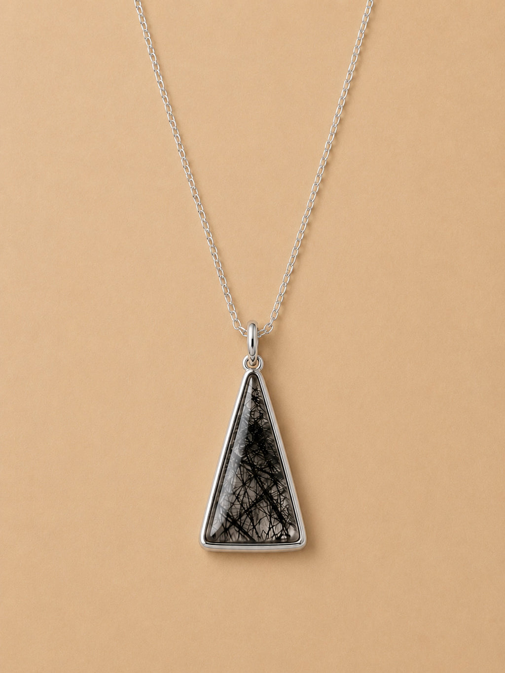 Sterling silver necklace with Triangular tourmalated quartz pendant on a beige background