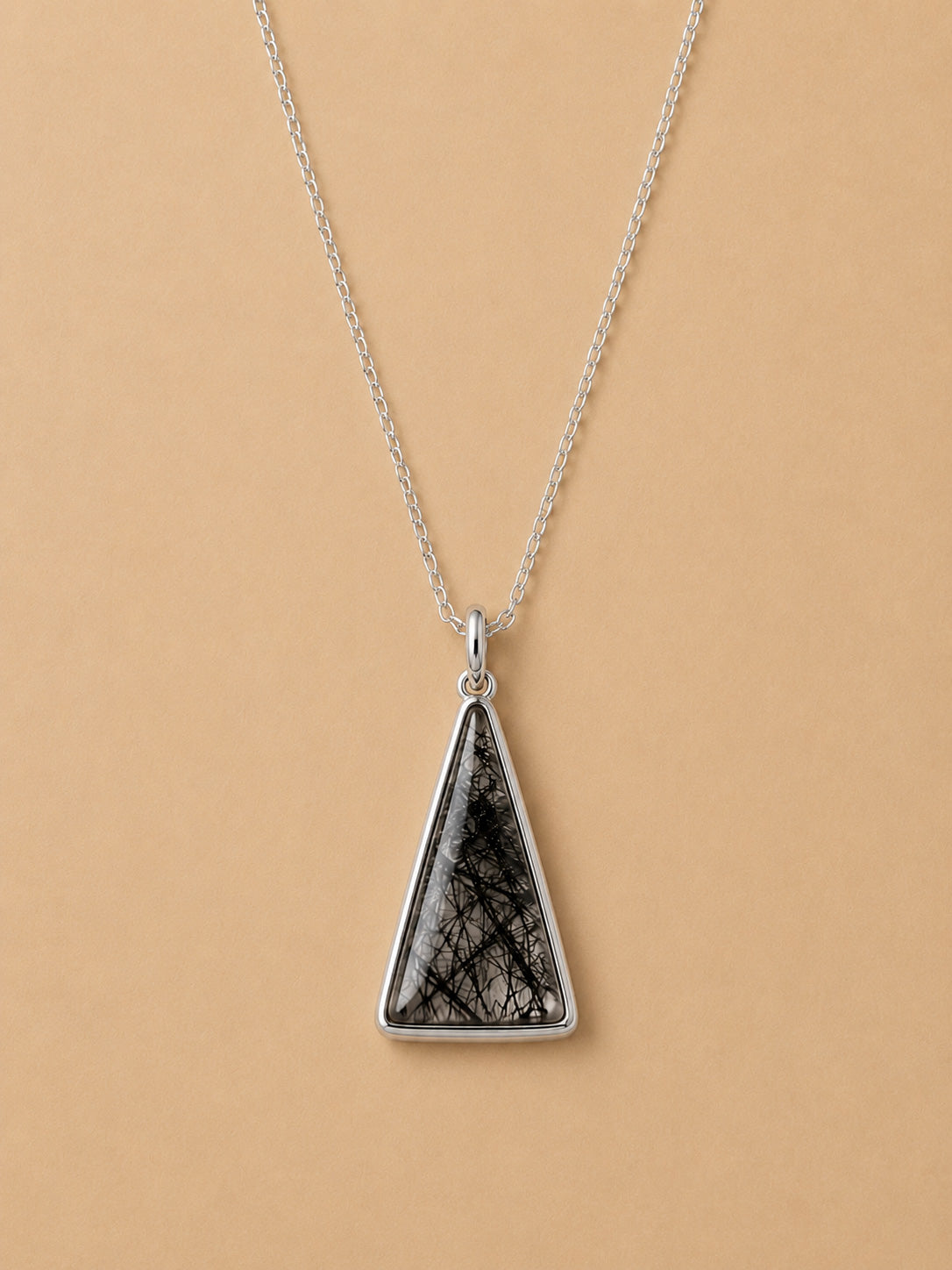 Sterling silver necklace with Triangular tourmalated quartz pendant on a beige background
