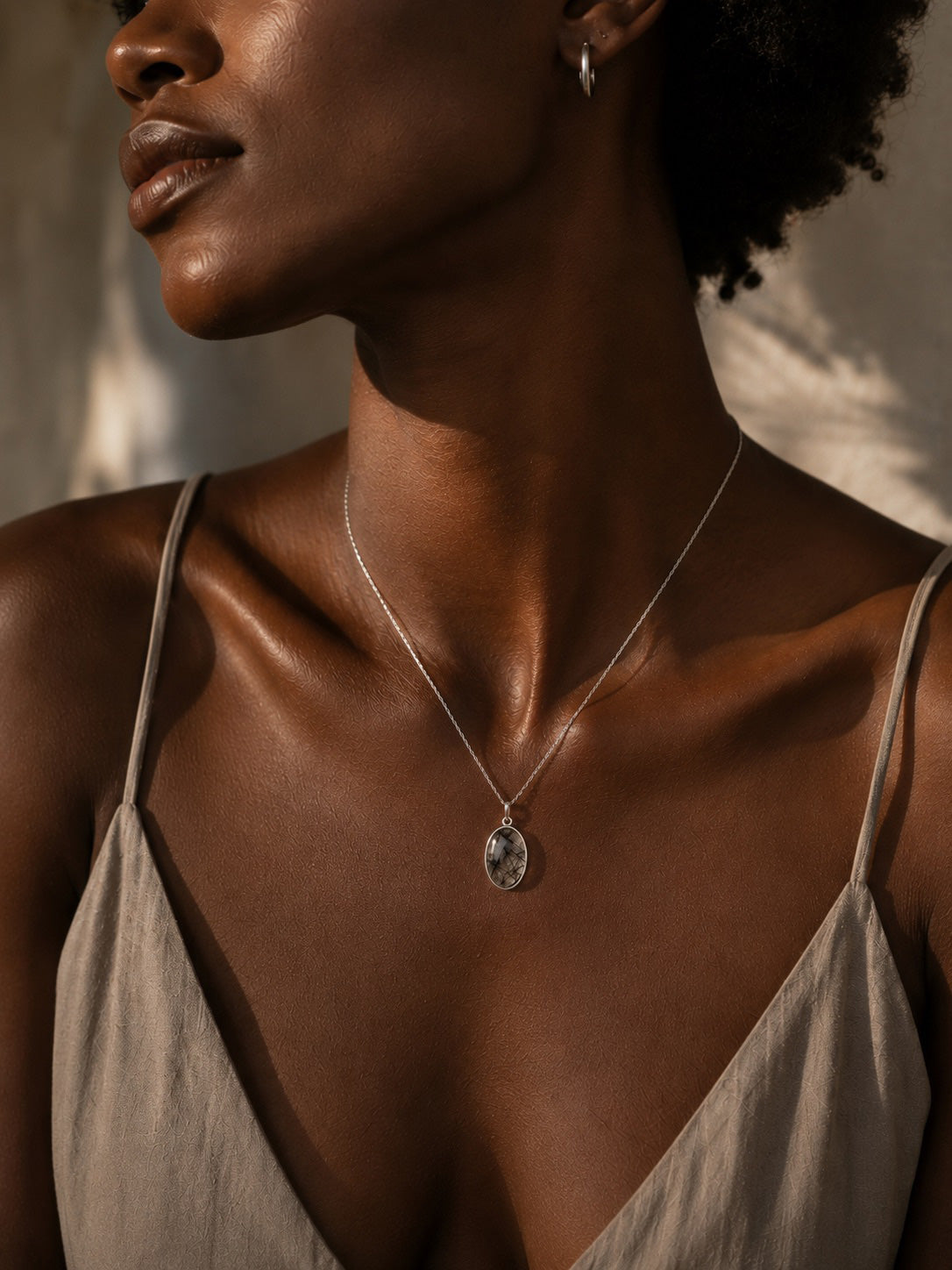 Close-up of a woman wearing a sterling silver necklace with a oval tourmalated quartz pendant against a neutral background.