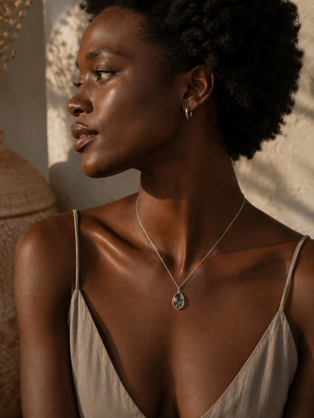 Woman wearing a sterling silver necklace with an oval tourmalated quartz pendant in a warm, softly lit setting
