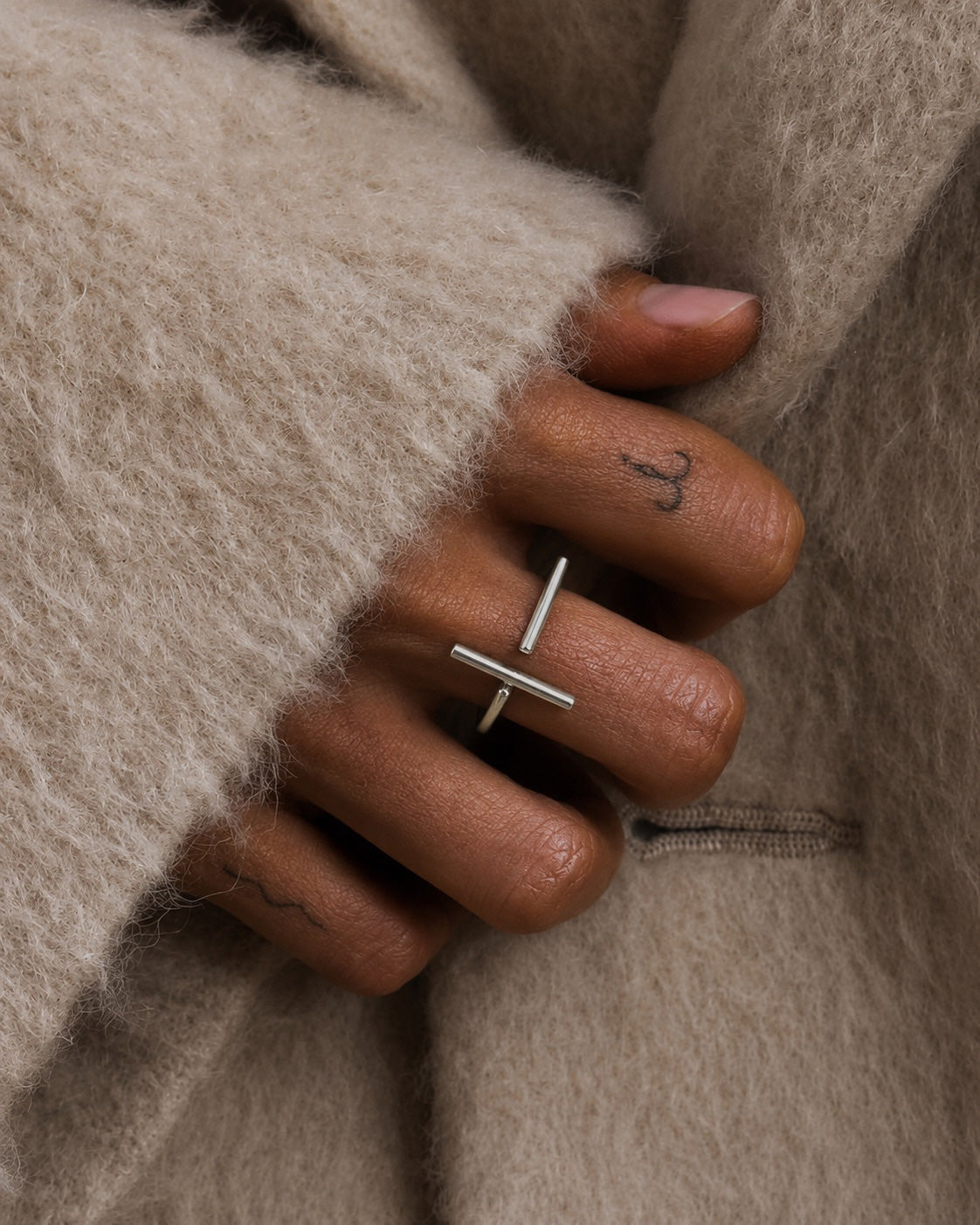 Close-up of a hand wearing a sterling silver ring with a contemporary minimalist broken bar design, by Ryā Atelier, wrapped in beige fabric.