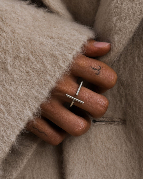 Close-up of a hand wearing a sterling silver ring with a contemporary minimalist broken bar design, by Ryā Atelier, wrapped in beige fabric.
