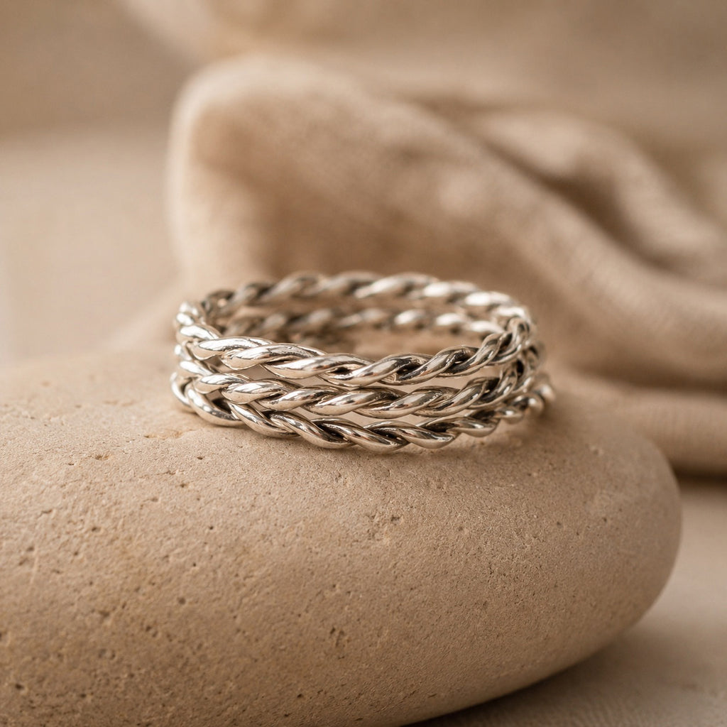 Three sterling Silver twisted rings on a beige stone surface