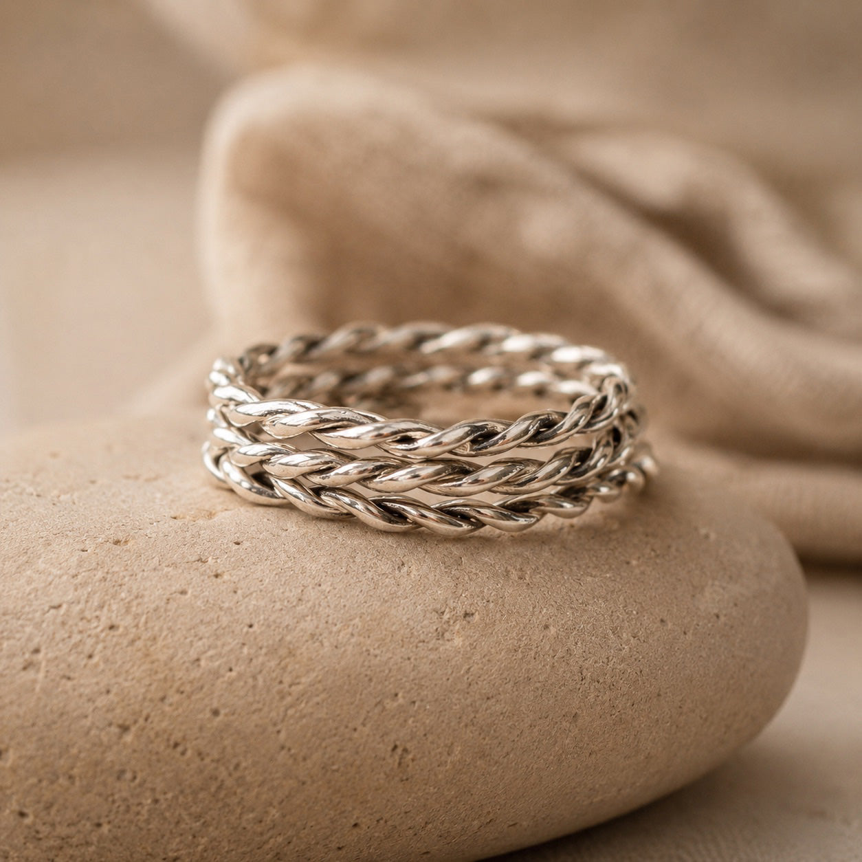 Three sterling Silver twisted rings on a beige stone surface