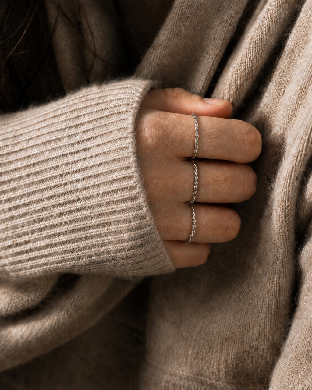 Close-up of a hand wearing three sterling silver twisted rings with a beige sweater.