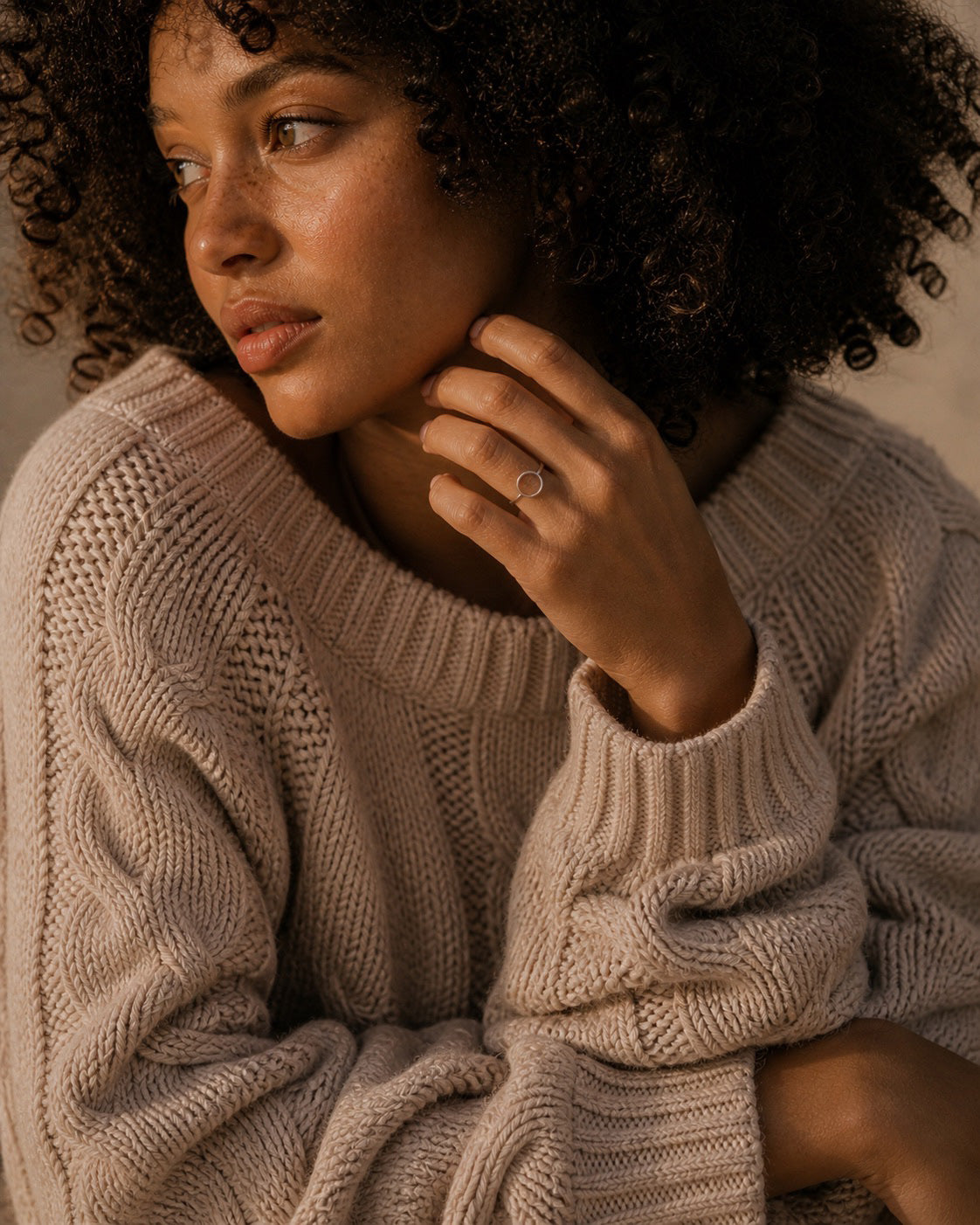 Woman wearing a sterling silver ring with a circle design and a beige knit sweater with a neutral background