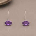 Pair of purple amethyst earrings set in sterling silver on a beige surface