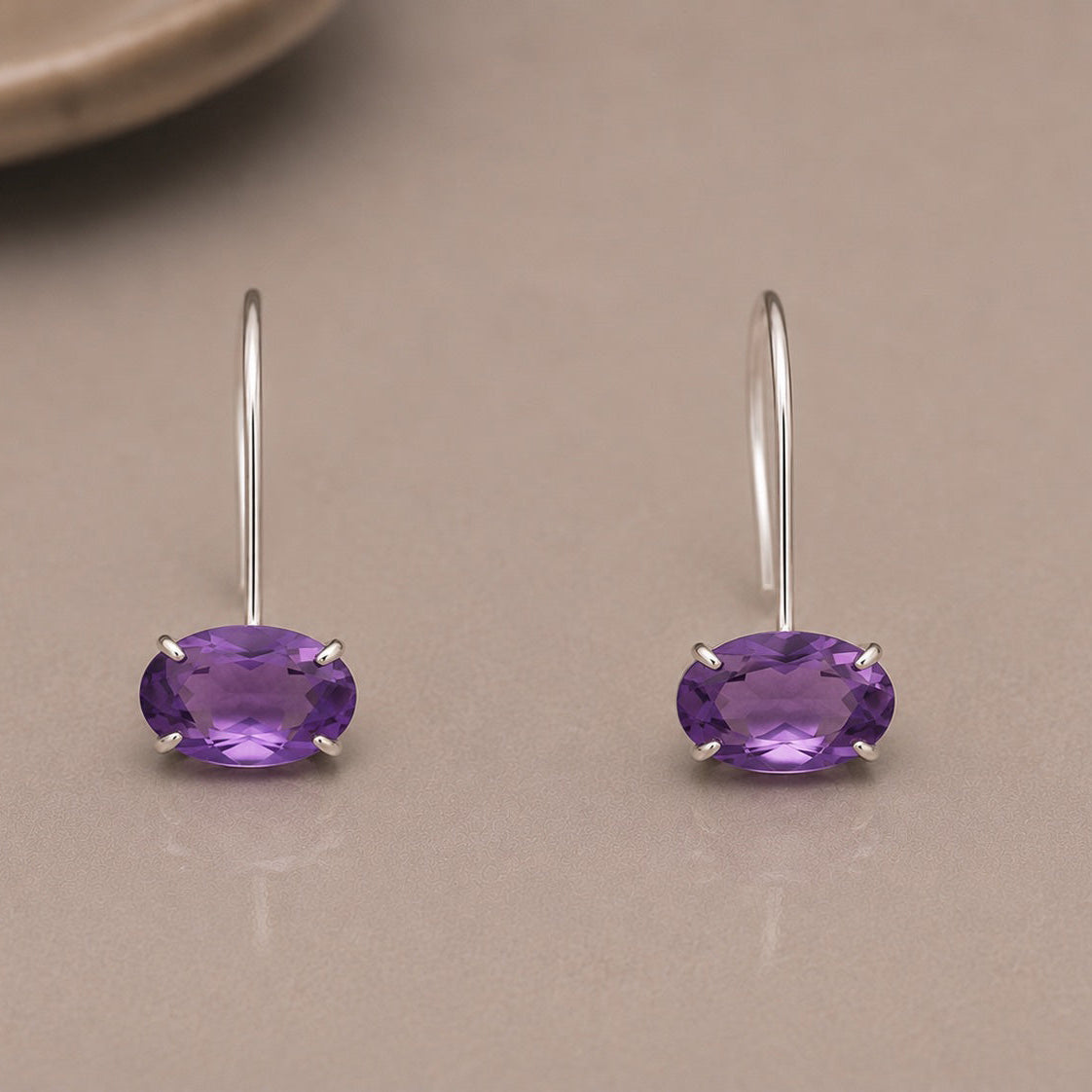 Pair of purple amethyst earrings set in sterling silver on a beige surface