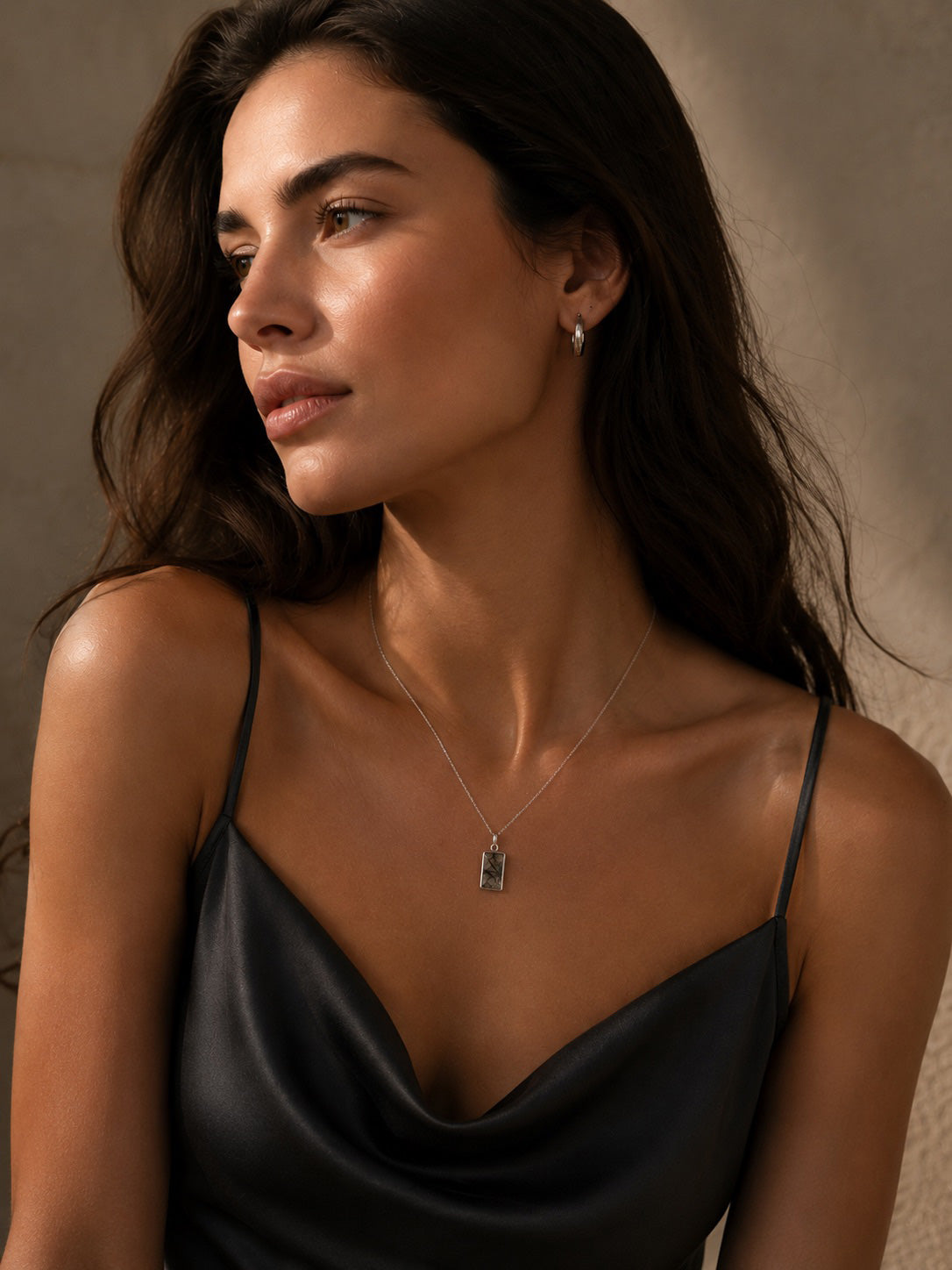 Woman wearing a black strappy top and a sterling silver necklace with a tourmalated Quartz pendant against a neutral background