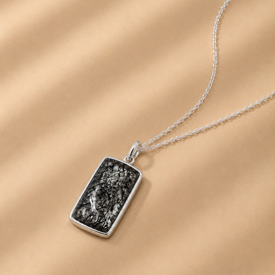 Sterling Silver necklace with a rectangular natural Tourmalated Quartz pendant on a beige background