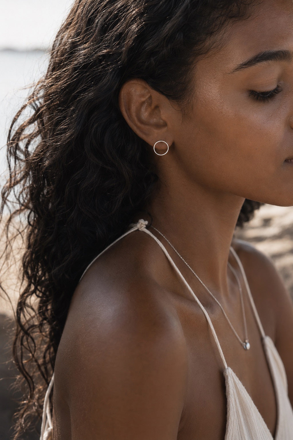 Close-up of a woman wearing a sterling silver earring and necklace on a blurred beach background