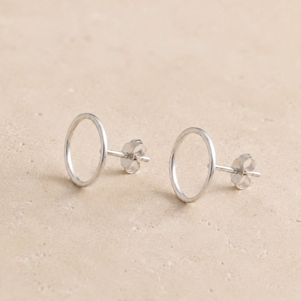Pair of sterling silver circle stud earrings on a beige background
