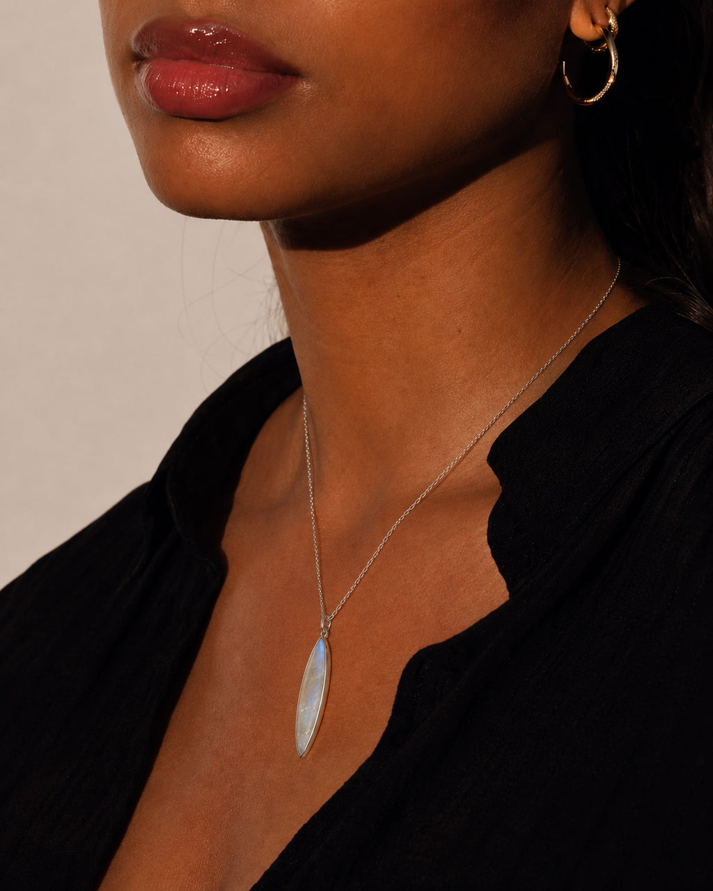 Close-up of a person wearing a necklace with a marquise-shaped moonstone pendant against a neutral background
