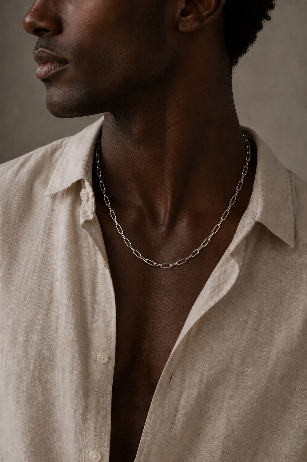 Man wearing a beige shirt and sterling silver paperclip chain necklace against a neutral background